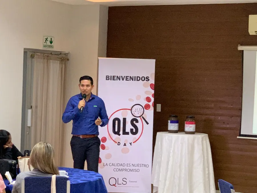 Expositor con micrófono junto al banner del QLS Day